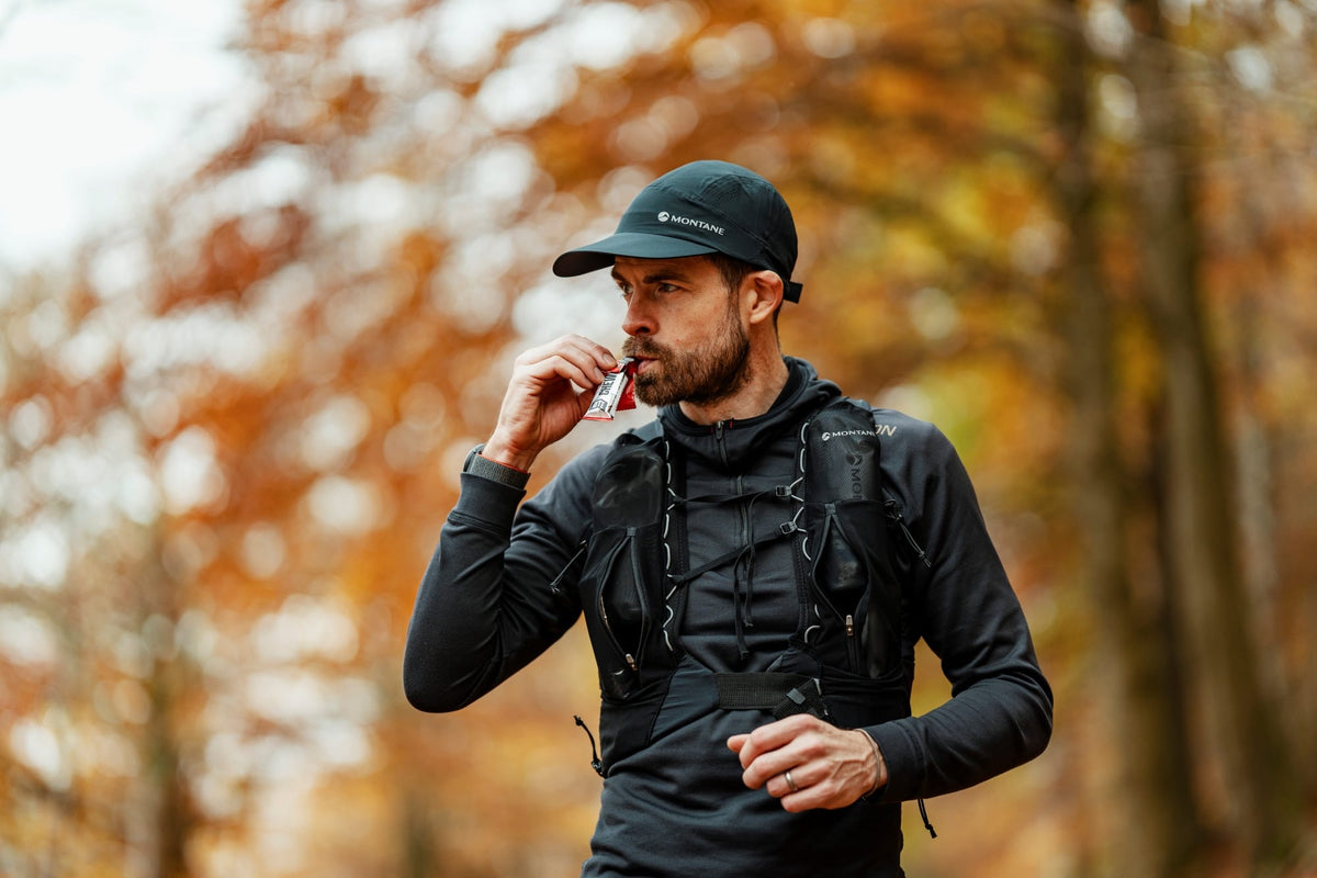 Man in black athletic wear and cap drinking from a bottle in an autumn forest.
