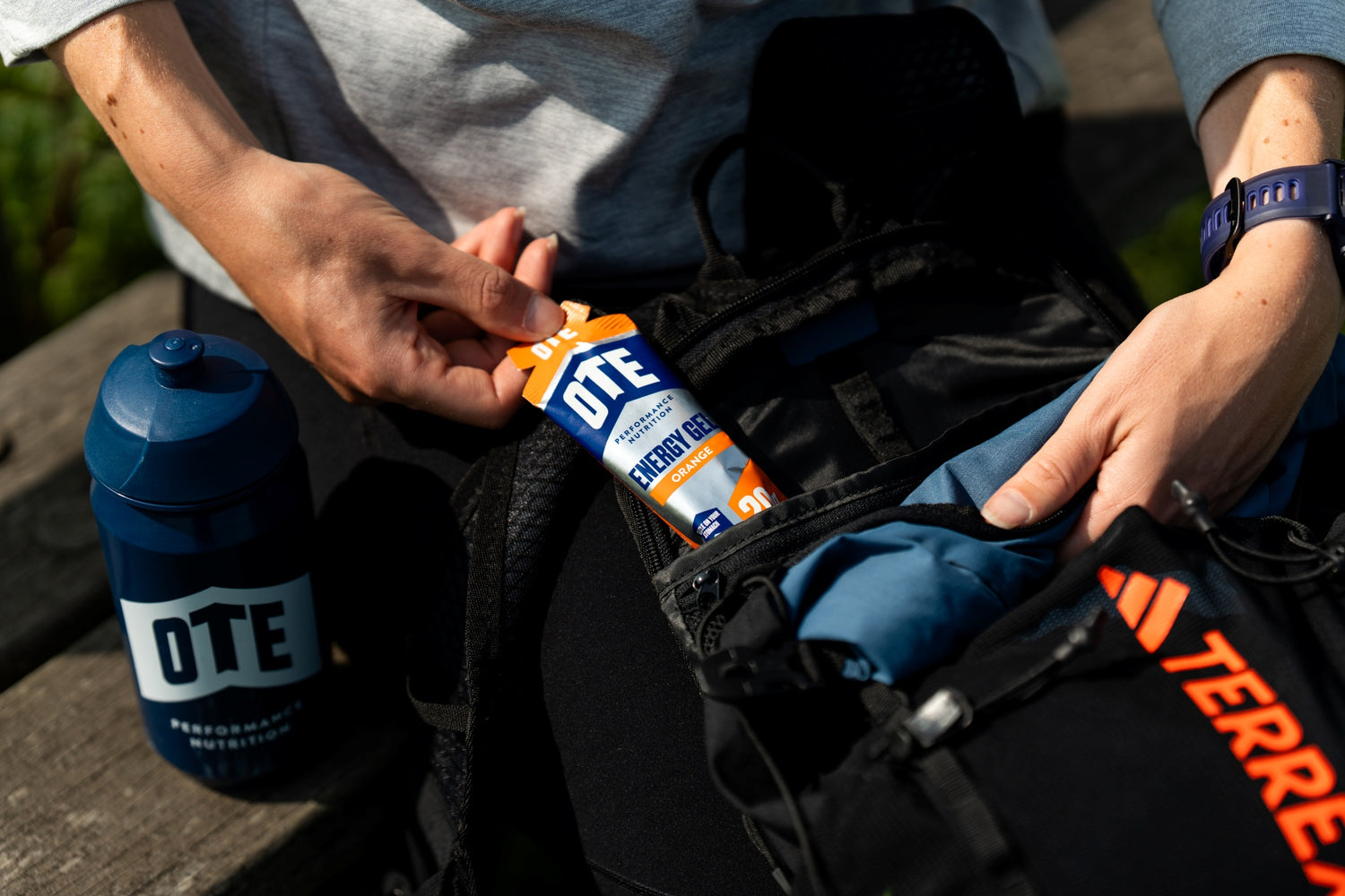 Person packing OTE sports drink mix into a backpack with a water bottle nearby
