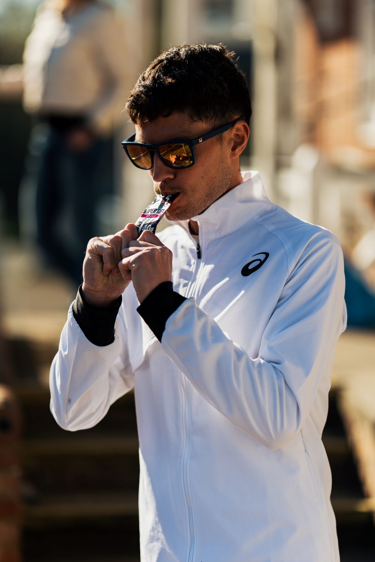 Person wearing a white jacket with a brand logo, holding a sports bottle.