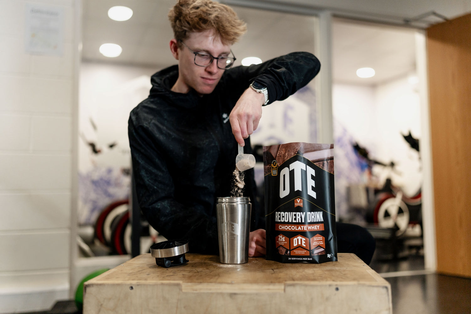 Person preparing a drink with OTE Recovery Drink mix in a gym setting