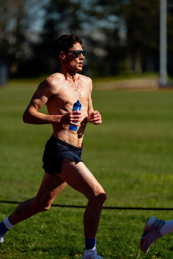 Man running shirtless on a grassy field holding a water bottle