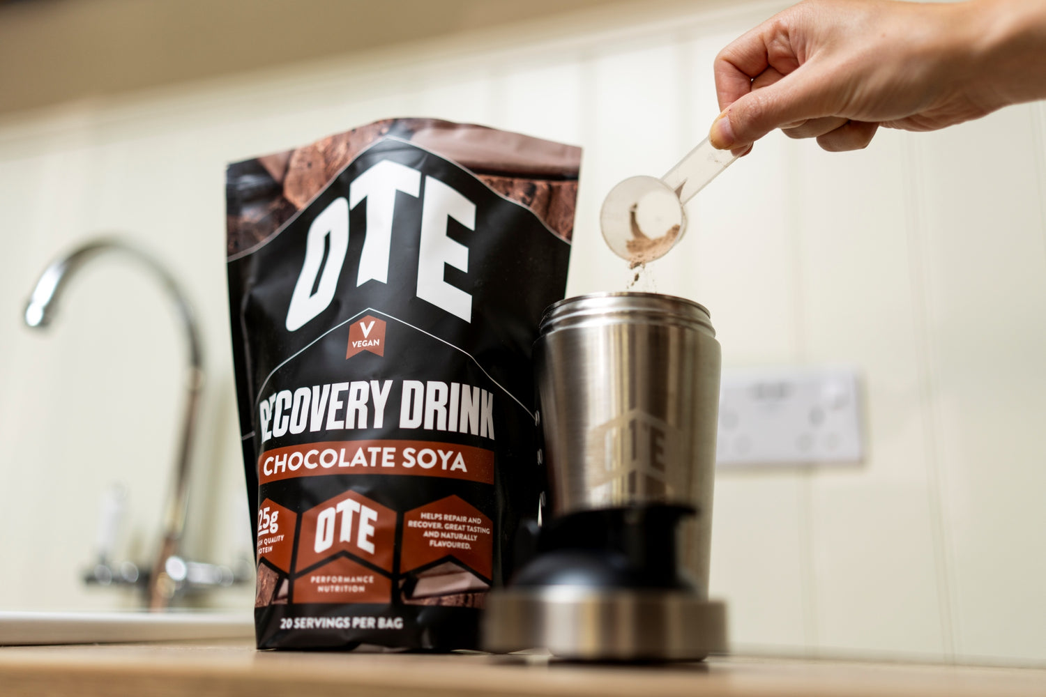 OTE Recovery Drink Chocolate Soya being poured into a container with a kitchen background.