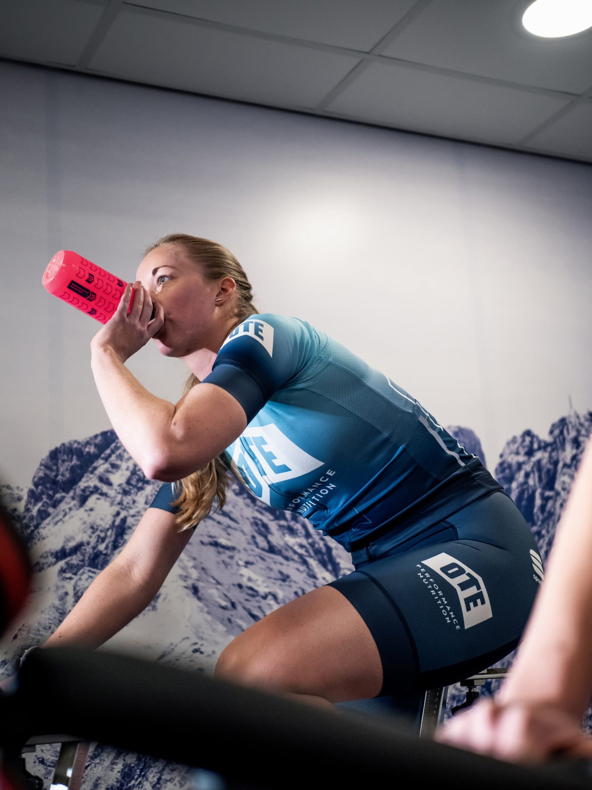 Cyclist drinking from an OTE Sports bottle while indoor training.