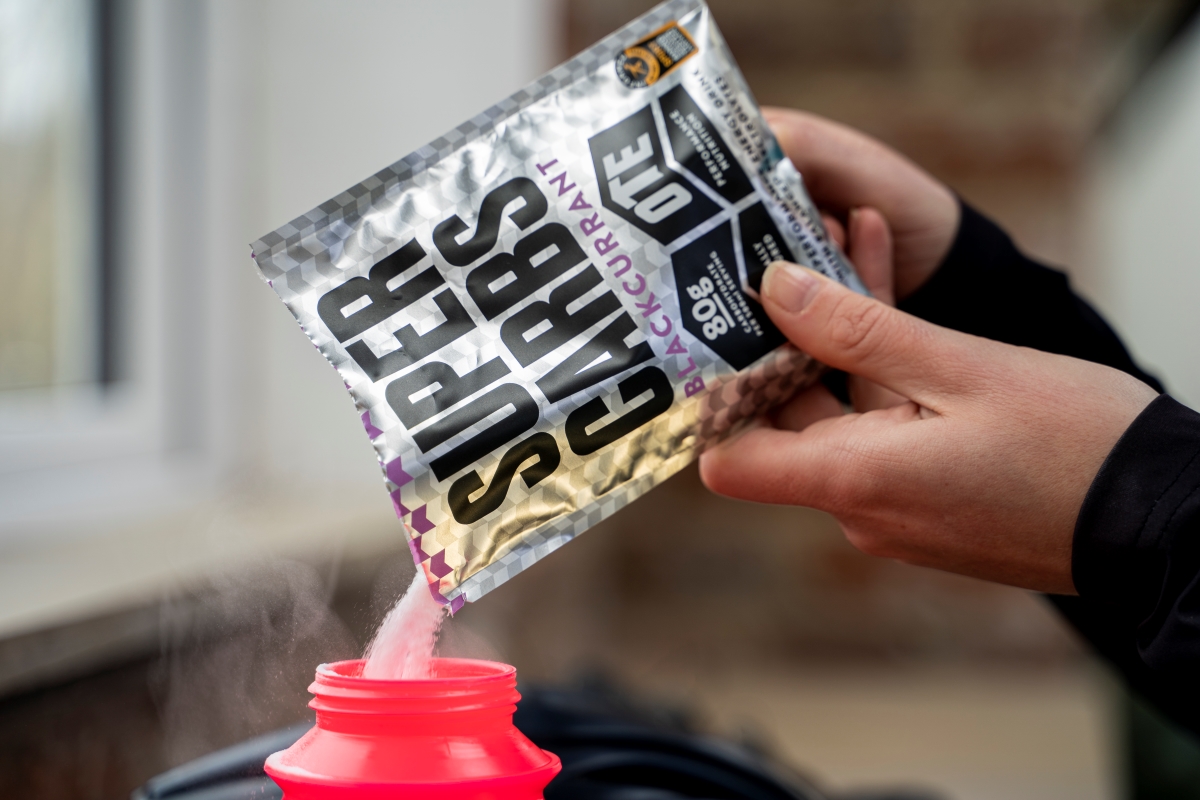 Pouring OTE Sports super carbs powder into a water bottle.